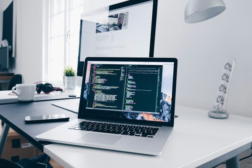 Software developer workspace with laptop displaying code, reference notes and a creative work area